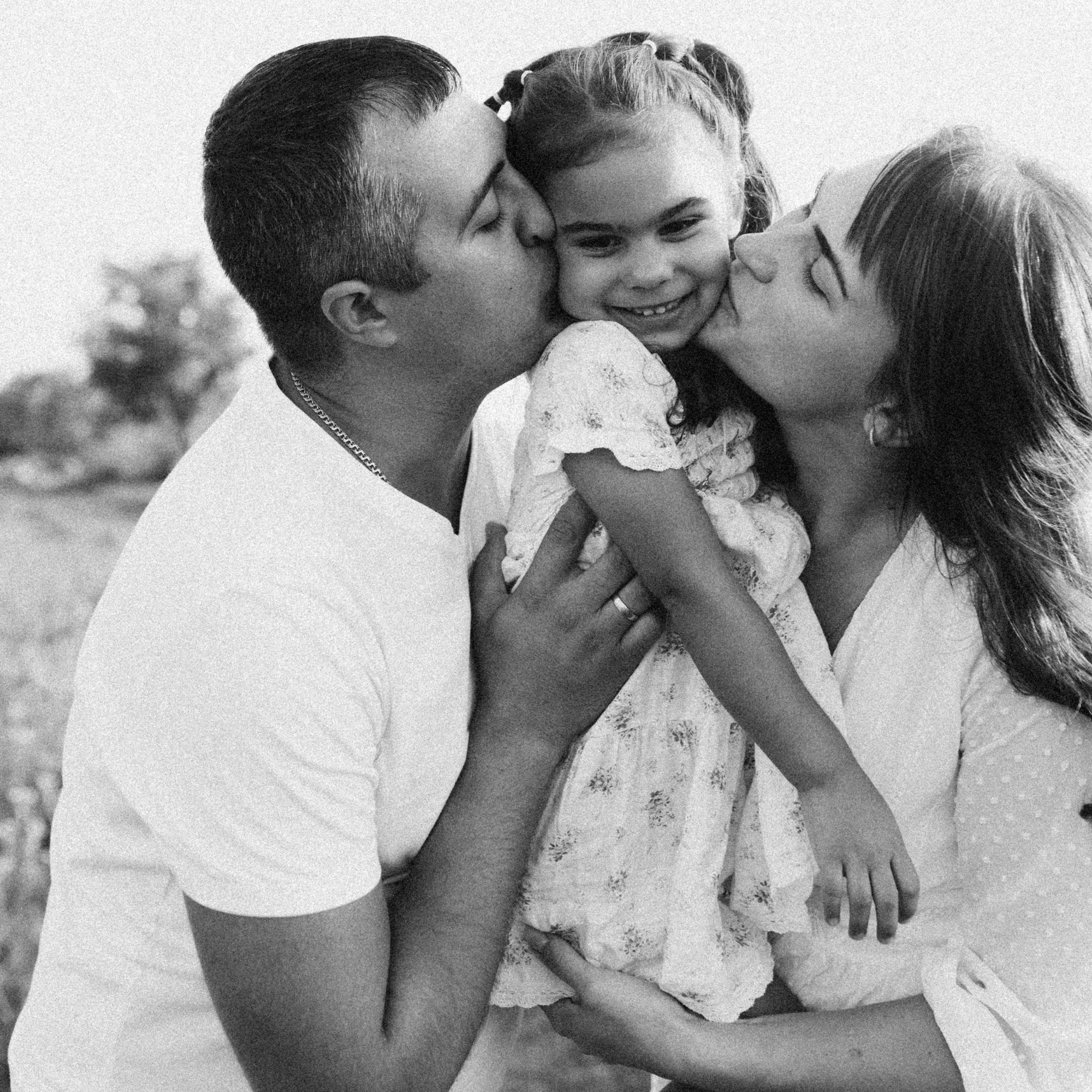 mom and dad smother daughter with kisses